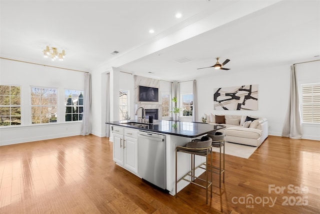 kitchen featuring dark countertops, a large fireplace, open floor plan, dishwasher, and a sink