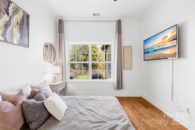 bedroom with crown molding, wood finished floors, visible vents, and baseboards