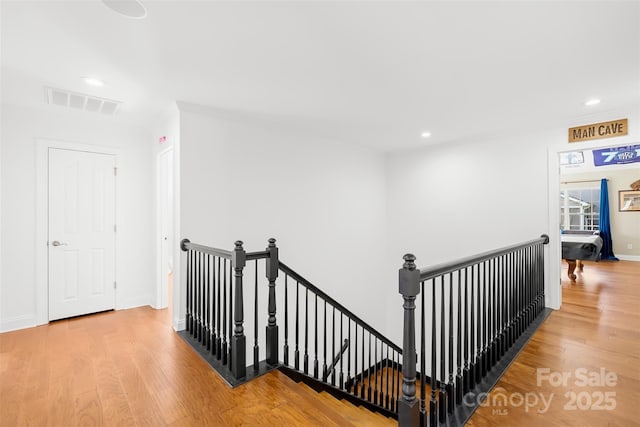 hallway with wood finished floors, an upstairs landing, and visible vents