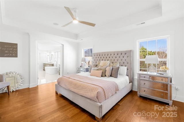 bedroom with a tray ceiling, wood finished floors, visible vents, and baseboards