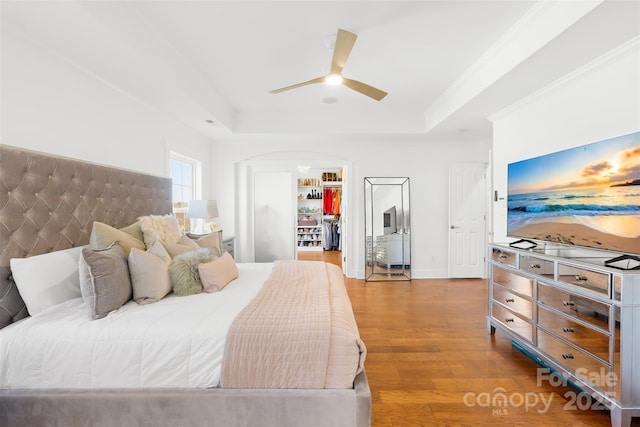 bedroom featuring a tray ceiling, crown molding, a spacious closet, and wood finished floors