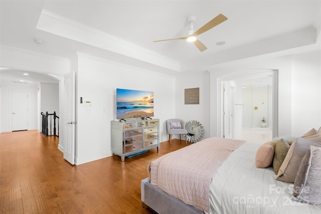 bedroom featuring baseboards, a tray ceiling, ornamental molding, wood finished floors, and a ceiling fan