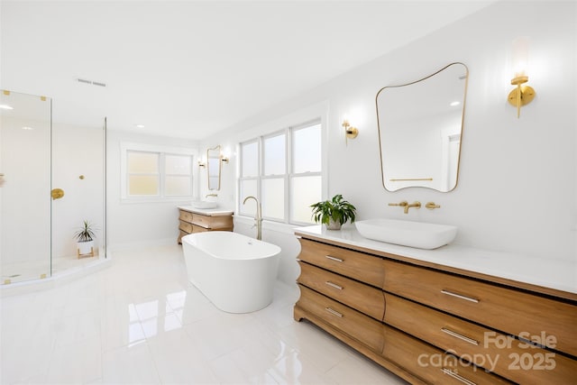 full bathroom featuring visible vents, a freestanding bath, two vanities, an enclosed shower, and a sink