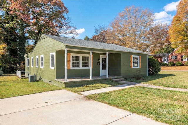 bungalow-style home featuring central AC unit, covered porch, a front yard, and roof with shingles