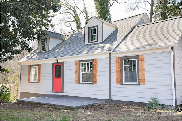 new england style home with a patio and roof with shingles