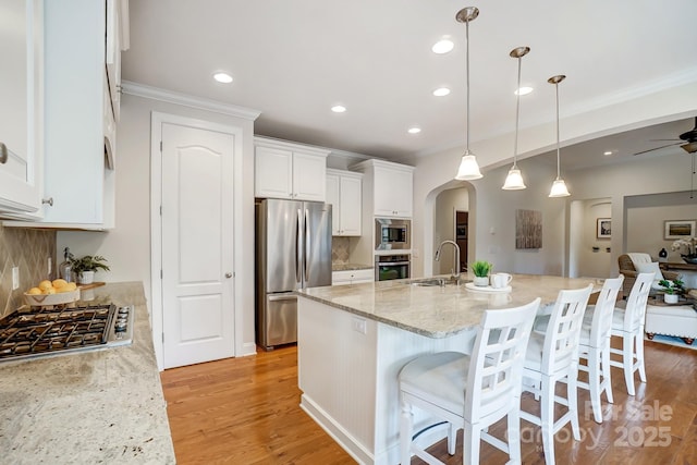 kitchen with arched walkways, stainless steel appliances, a sink, white cabinets, and light wood-style floors