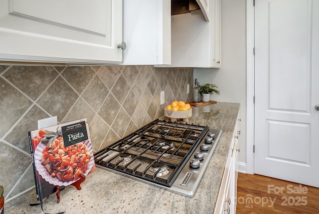 kitchen with light stone countertops, stainless steel gas stovetop, white cabinetry, and decorative backsplash