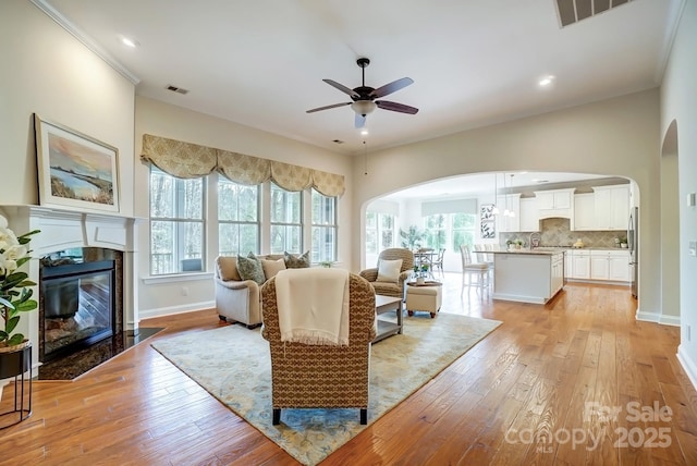 living area featuring light wood-type flooring, a fireplace with flush hearth, and visible vents