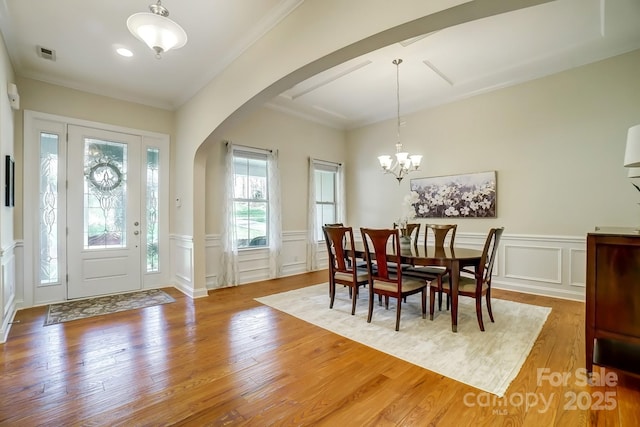 entrance foyer featuring arched walkways, visible vents, a decorative wall, a chandelier, and hardwood / wood-style floors