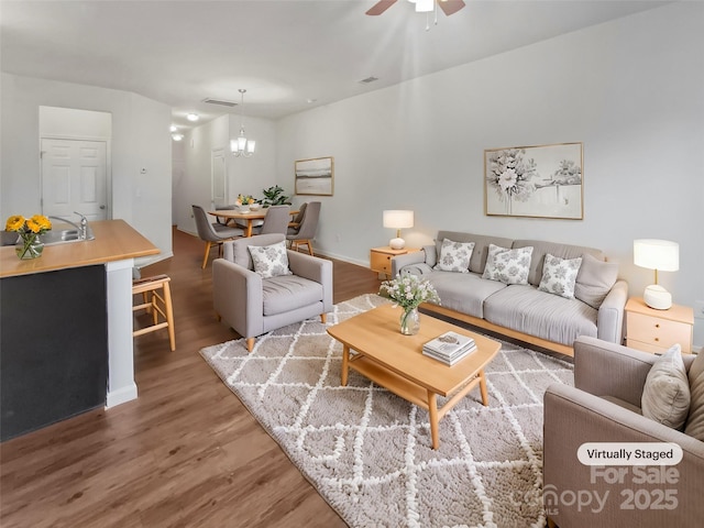 living area featuring ceiling fan with notable chandelier, visible vents, baseboards, and wood finished floors