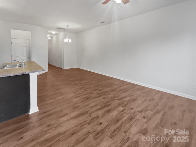 unfurnished living room featuring visible vents, a sink, wood finished floors, baseboards, and ceiling fan with notable chandelier