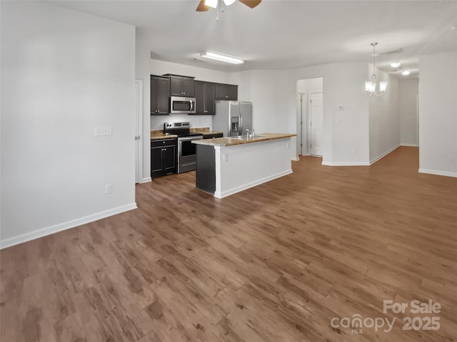 kitchen featuring open floor plan, stainless steel appliances, ceiling fan with notable chandelier, and wood finished floors