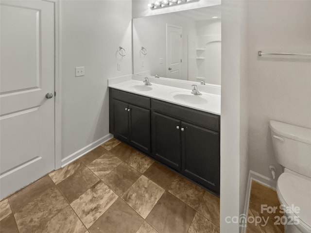 bathroom featuring toilet, double vanity, baseboards, and a sink