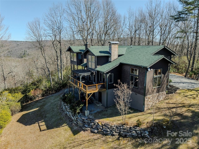 back of property featuring a wooden deck, roof with shingles, dirt driveway, and a chimney