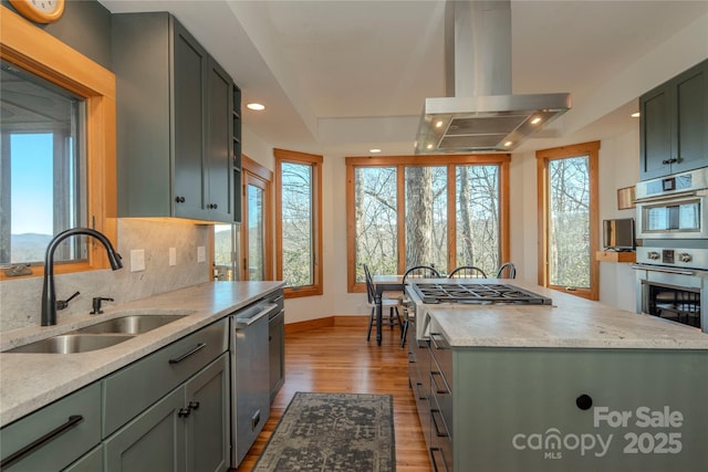 kitchen featuring tasteful backsplash, dishwasher, island exhaust hood, wood finished floors, and a sink