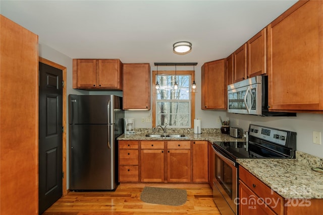 kitchen with a sink, light stone countertops, appliances with stainless steel finishes, and brown cabinetry