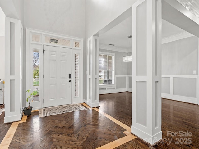 entryway featuring crown molding, a wainscoted wall, a decorative wall, and a high ceiling