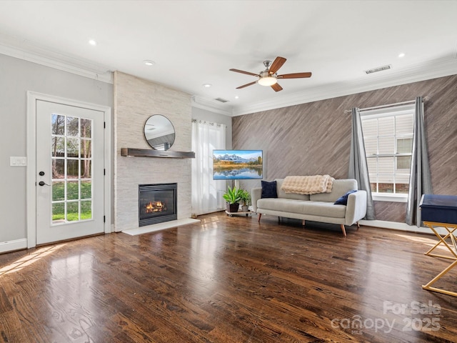 unfurnished living room featuring a stone fireplace, wood finished floors, visible vents, baseboards, and crown molding