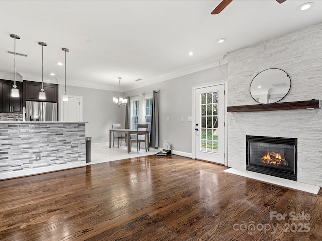 unfurnished living room featuring visible vents, ornamental molding, wood finished floors, a fireplace, and ceiling fan with notable chandelier