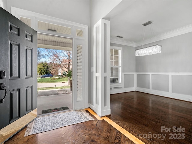 foyer with visible vents, a wainscoted wall, wood finished floors, crown molding, and a decorative wall