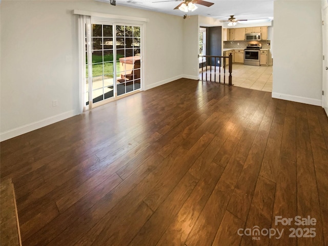 unfurnished living room featuring wood-type flooring, a ceiling fan, and baseboards