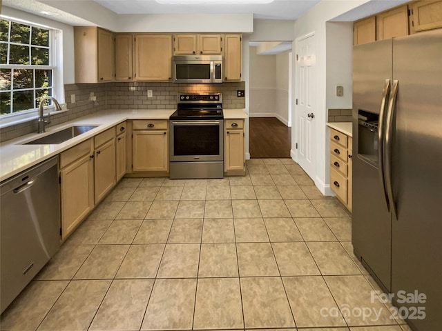 kitchen featuring light tile patterned floors, stainless steel appliances, a sink, light countertops, and decorative backsplash