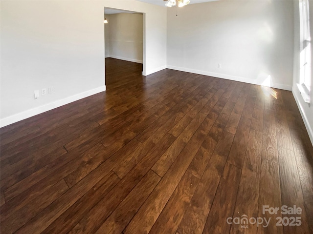 unfurnished room with a ceiling fan, baseboards, and dark wood-type flooring