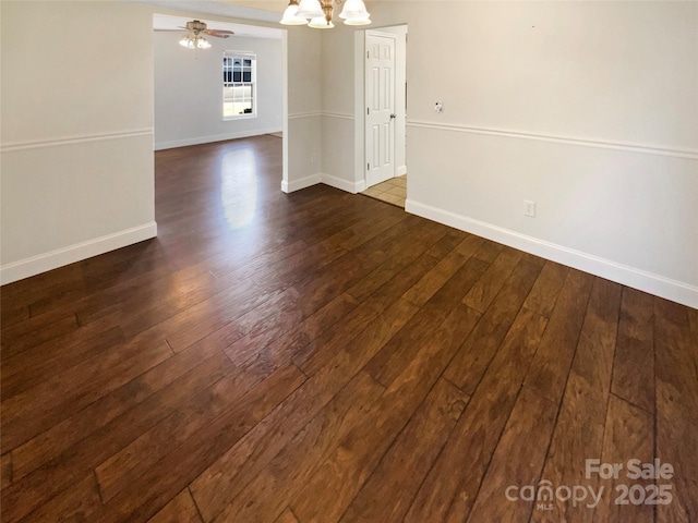 unfurnished dining area with ceiling fan with notable chandelier, dark wood-type flooring, and baseboards