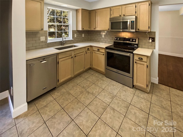 kitchen featuring light countertops, decorative backsplash, appliances with stainless steel finishes, a sink, and baseboards