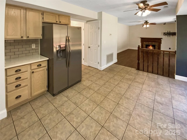 kitchen featuring a warm lit fireplace, visible vents, light countertops, decorative backsplash, and stainless steel fridge