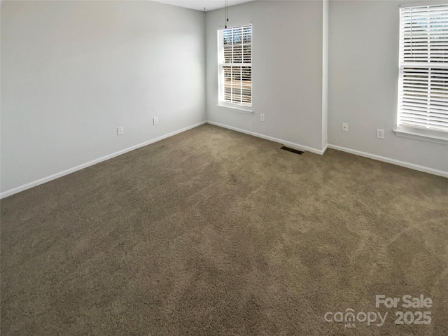 empty room with baseboards, visible vents, and dark carpet