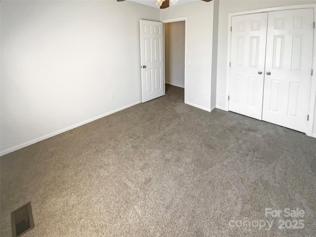 unfurnished bedroom featuring a closet, visible vents, dark carpet, a ceiling fan, and baseboards