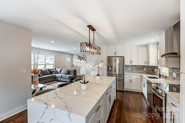 kitchen featuring a sink, open floor plan, wall chimney range hood, appliances with stainless steel finishes, and a center island