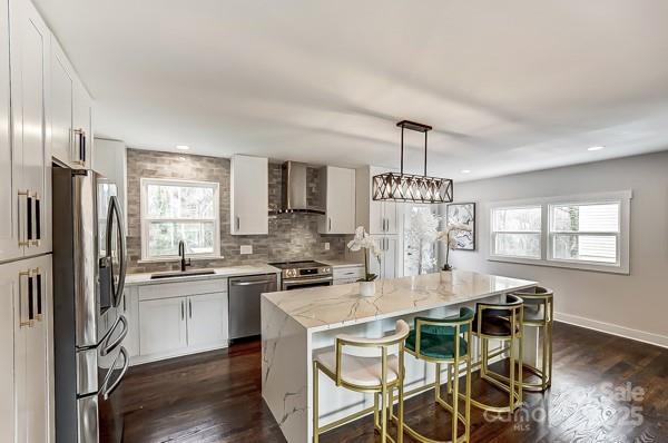 kitchen with stainless steel appliances, wall chimney exhaust hood, a sink, and a wealth of natural light