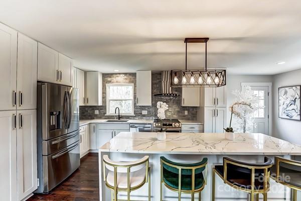 kitchen with tasteful backsplash, wall chimney exhaust hood, a breakfast bar area, stainless steel appliances, and a sink