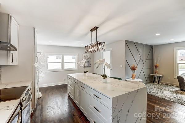 kitchen featuring wall chimney exhaust hood, stainless steel electric range, light stone counters, and dark wood-type flooring