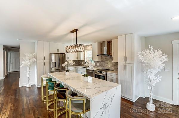 kitchen featuring light stone counters, stainless steel appliances, backsplash, a center island, and wall chimney exhaust hood