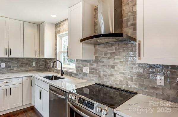 kitchen with wall chimney exhaust hood, white cabinetry, stainless steel appliances, and a sink