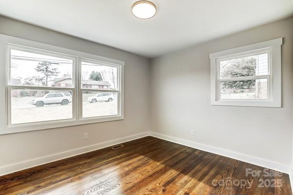 spare room with dark wood-style flooring, visible vents, and baseboards