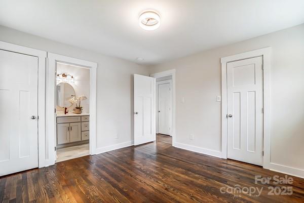 unfurnished bedroom featuring connected bathroom, baseboards, and dark wood-style flooring