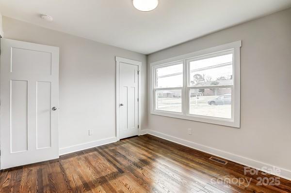 unfurnished bedroom with dark wood-style flooring, visible vents, and baseboards