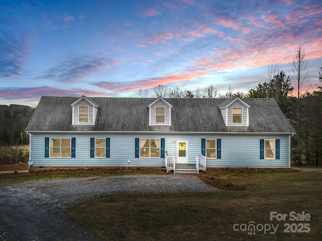 cape cod-style house featuring a front yard, roof with shingles, and driveway