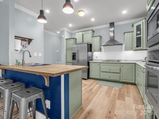 kitchen with green cabinets, stainless steel appliances, wall chimney exhaust hood, and a sink