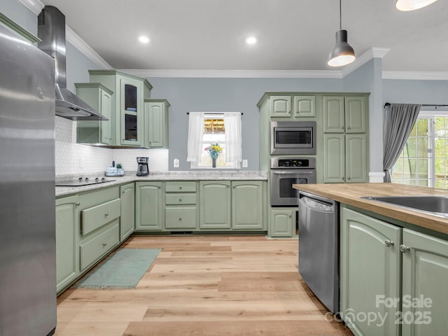 kitchen with green cabinets, wall chimney range hood, light wood finished floors, and appliances with stainless steel finishes