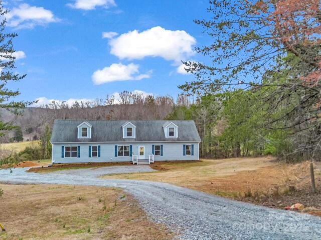 view of front facade with a front yard, a forest view, and driveway