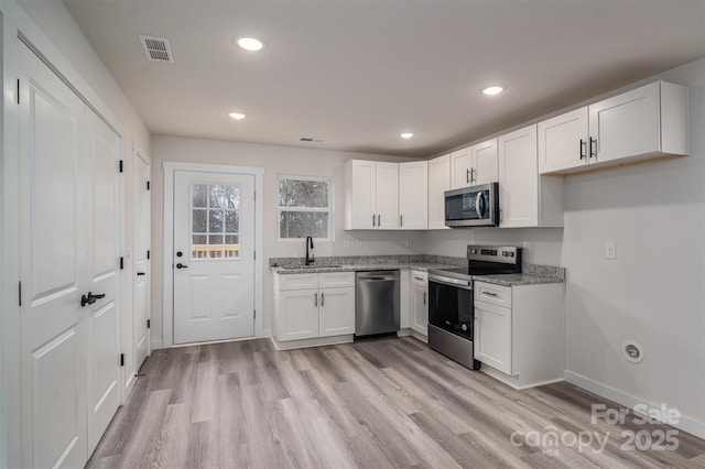 kitchen featuring light wood finished floors, appliances with stainless steel finishes, white cabinetry, a sink, and light stone countertops