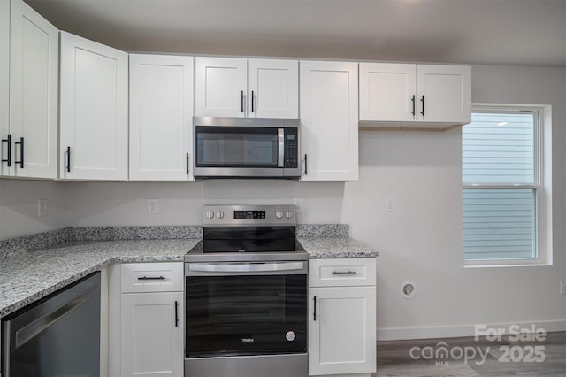 kitchen featuring baseboards, stainless steel appliances, white cabinetry, and light stone countertops