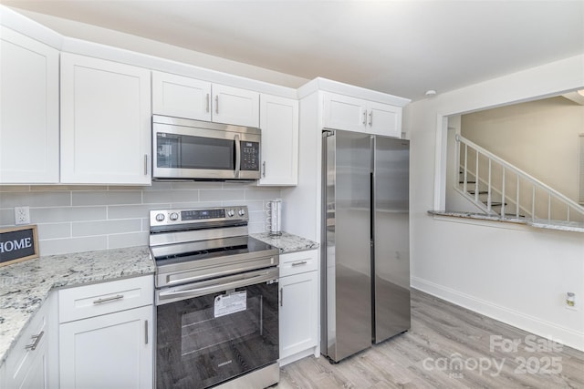 kitchen with stainless steel appliances, light wood finished floors, backsplash, and white cabinets