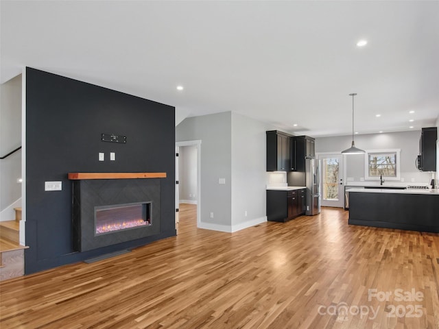 unfurnished living room with baseboards, a glass covered fireplace, stairway, light wood-style floors, and recessed lighting