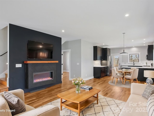 living room featuring light wood-type flooring, recessed lighting, stairs, and a glass covered fireplace